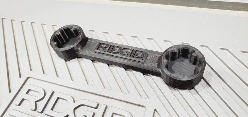 以下が含まれることがあります： ハンドルに「RIDGID」という文字が刻印された黒いプラスチック製のレンチ。レンチは両端に異なるサイズのソケットが2つあります。