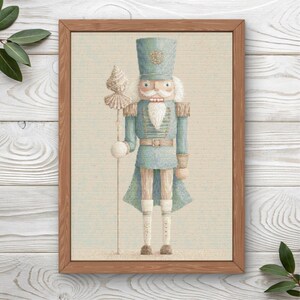 May include: A framed wall art print featuring a light blue nutcracker soldier wearing a tall hat and uniform with gold accents. The figure holds a tall staff topped with a seashell and has a white beard, standing against a textured background.