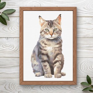 May include: A framed print featuring a detailed illustration of a tabby cat. The cat is depicted in shades of gray, brown, and tan, with green eyes and a focused gaze. The artwork is set against a white background and framed in a natural wood.