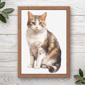 May include: A framed print featuring a detailed watercolor-style image of a seated tabby cat. The cat has brown, white, and tan fur, with yellow eyes and long whiskers. The artwork is set against a white background and framed in a light brown wooden frame.