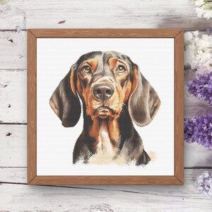 Peut inclure: Portrait encadré au point de croix d'un chien, représentant un chien marron et noir avec de longues oreilles tombantes et une expression mélancolique. L'œuvre est encadrée dans un cadre en bois naturel, mettant en valeur un design de broderie détaillé.
