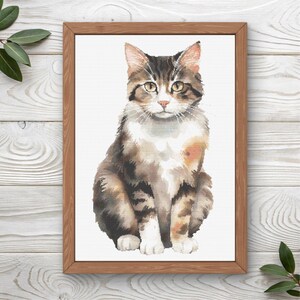 Puede incluir: Una impresión en acuarela enmarcada de un gato atigrado. El gato tiene pelaje marrón, blanco y canela, con ojos amarillos y nariz rosa. La obra de arte está sobre un fondo blanco y enmarcada en un marco de madera marrón claro.