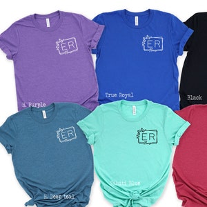 May include: Six t-shirts in different colors with the letters "ER" in a white frame with floral accents. The colors are hi purple, true royal, black, hi deep teal, tahiti blue, and red.