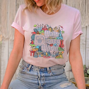 May include: A pink t-shirt featuring a colourful graphic of Walt Disney World landmarks and the text "Walt Disney World".