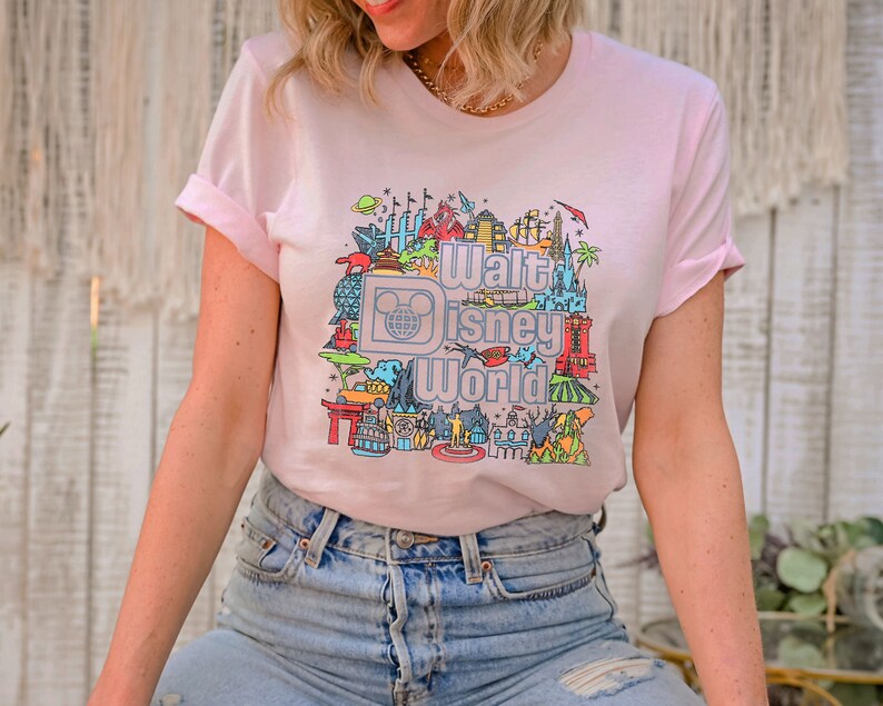 May include: A pink t-shirt featuring a colourful graphic of Walt Disney World landmarks and the text "Walt Disney World".