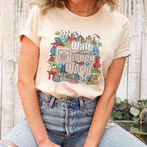 May include: A beige t-shirt featuring a colourful graphic print of Walt Disney World landmarks and the text "Walt Disney World".