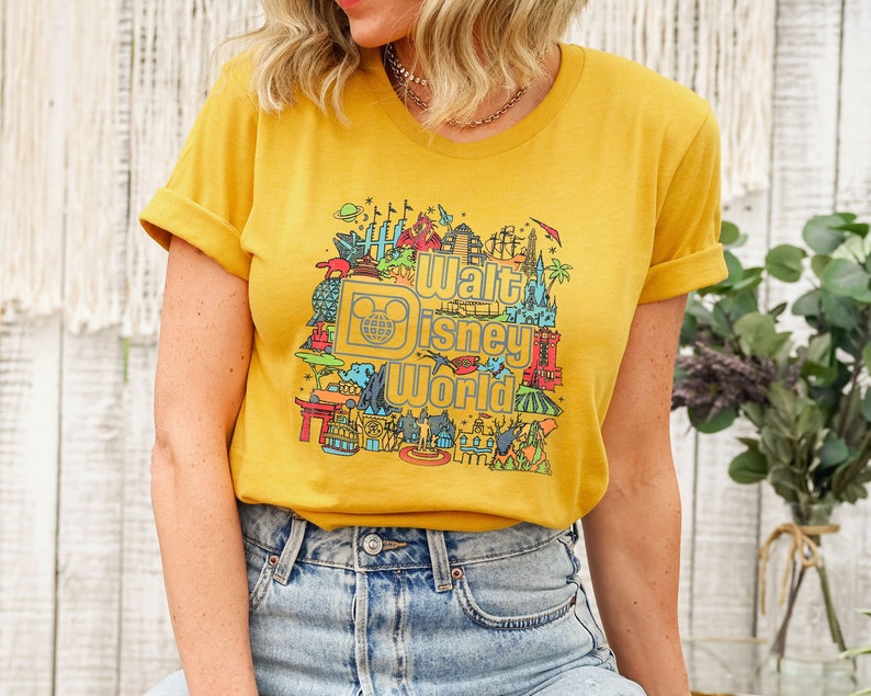 May include: A yellow t-shirt featuring a colourful graphic of Walt Disney World landmarks and the text "Walt Disney World".
