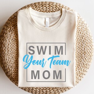 K&ouml;nnte beinhalten: Ein wei&szlig;es T-Shirt mit dem Text "SWIM YOUR TEAM MOM" in einem blauen und grauen Kasten.