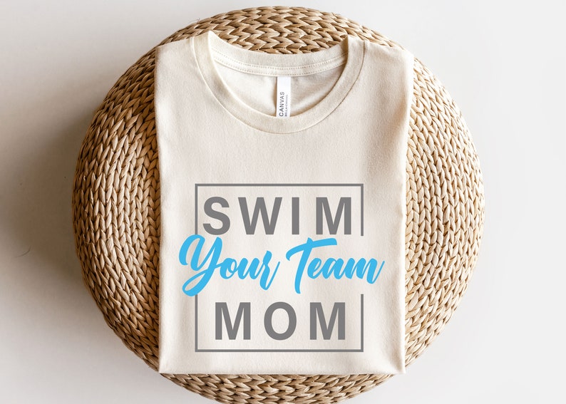 K&ouml;nnte beinhalten: Ein wei&szlig;es T-Shirt mit dem Text "SWIM YOUR TEAM MOM" in einem blauen und grauen Kasten.