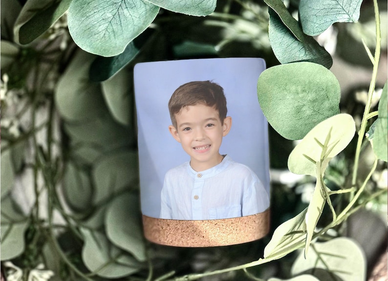 May include: A light blue mug with a cork band around the top. A photo of a young boy with brown hair is printed on the mug.