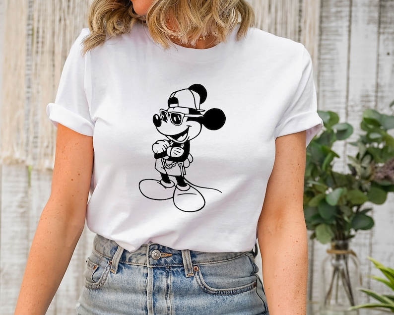 May include: White t-shirt featuring a black and white illustration of Mickey Mouse wearing sunglasses and a baseball cap.