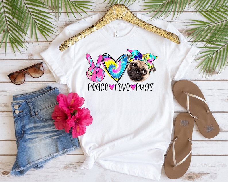 May include: White t-shirt with a tie-dye heart, peace sign, and a pug wearing a tie-dye headband. The text "Peace Love Pugs" is printed below the image.