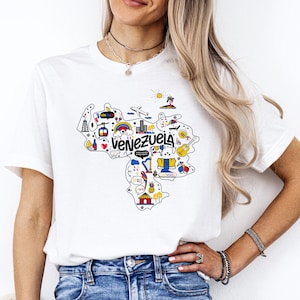 Może przedstawiać: Biała koszulka z kolorową grafiką Wenezueli, przedstawiającą zabytki, zwierzęta i napis "Venezuela".
