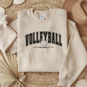 May include: A beige sweatshirt with the text "Volleyball Mom" in black with a volleyball graphic.