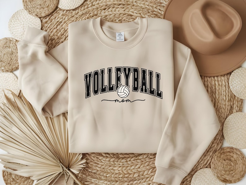 May include: A beige sweatshirt with the text "Volleyball Mom" in black with a volleyball graphic.
