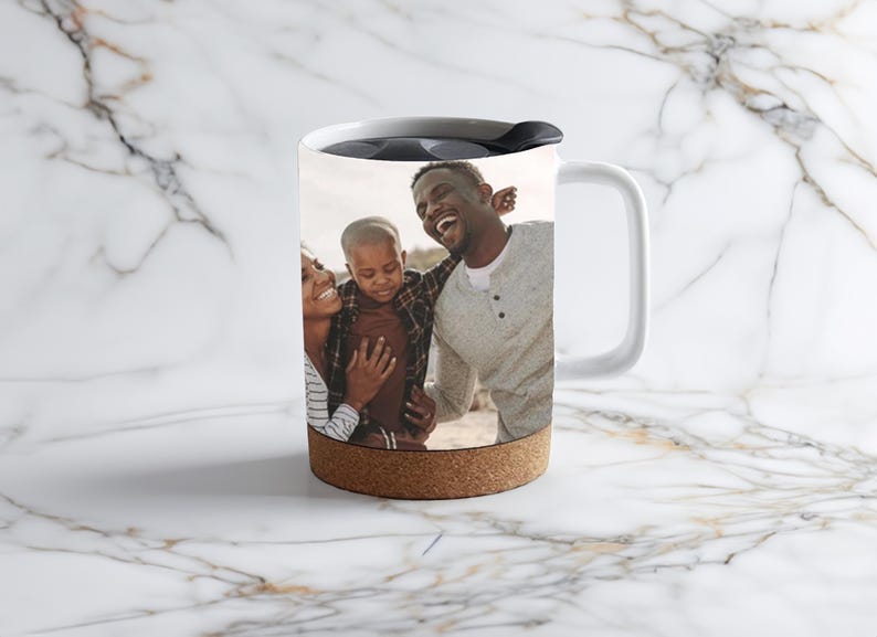 May include: White travel mug with a cork band and a photo of a family of three on the side. The photo shows a man, a woman, and a young boy smiling.