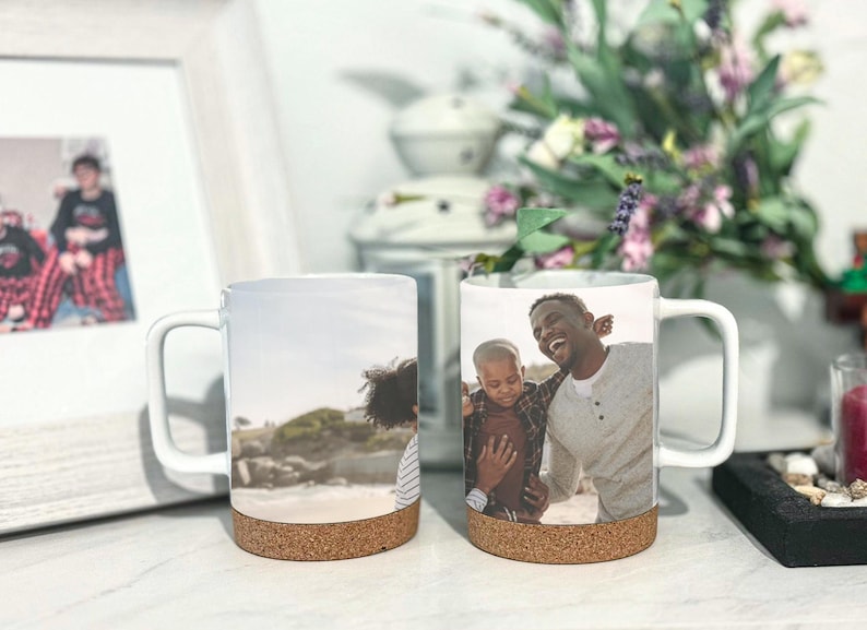May include: Two white ceramic mugs with cork bottoms. One mug features a photo of a father and son smiling at the beach. The other mug features a photo of a person with long brown hair looking at the beach.