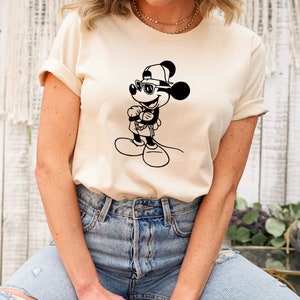 May include: A white t-shirt featuring a black and white illustration of Mickey Mouse wearing sunglasses and a baseball cap.