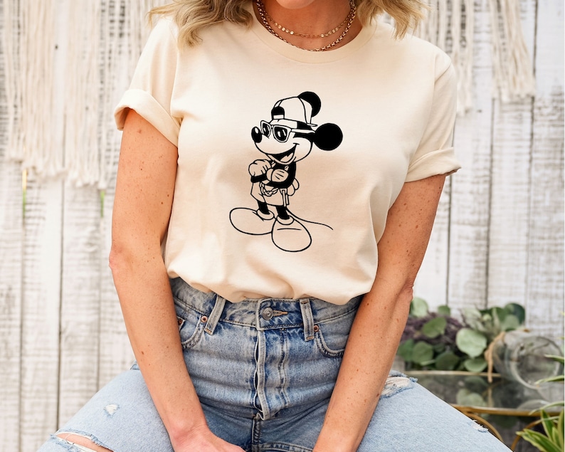May include: A white t-shirt featuring a black and white illustration of Mickey Mouse wearing sunglasses and a baseball cap.