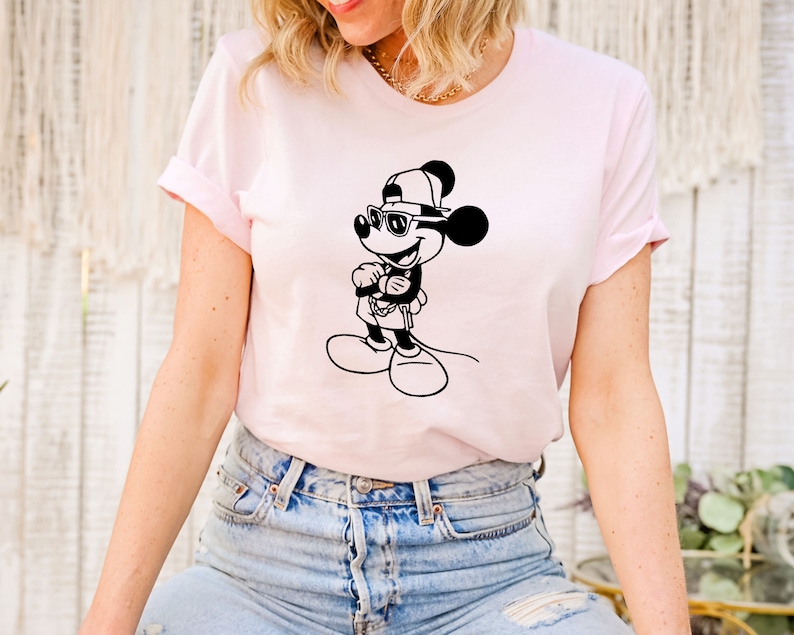 May include: A pink t-shirt featuring a black and white illustration of Mickey Mouse wearing sunglasses and a baseball cap.