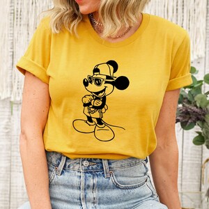 May include: A yellow t-shirt featuring a black and white illustration of Mickey Mouse wearing sunglasses and a baseball cap.