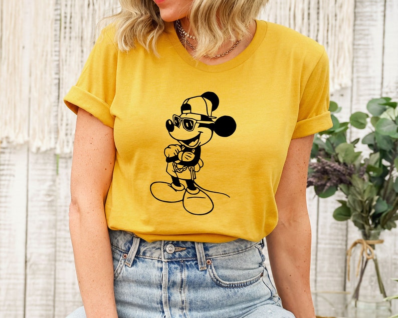 May include: A yellow t-shirt featuring a black and white illustration of Mickey Mouse wearing sunglasses and a baseball cap.