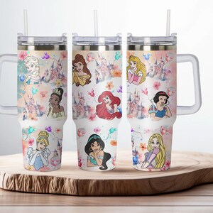 May include: Set of three stainless steel tumblers with a white background and colorful images of Disney princesses. The tumblers have a clear lid and a handle.