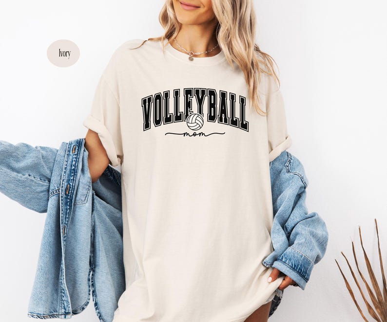 May include: A cream-colored t-shirt with the text "Volleyball Mom" in black lettering. A black and white volleyball graphic is included in the text.
