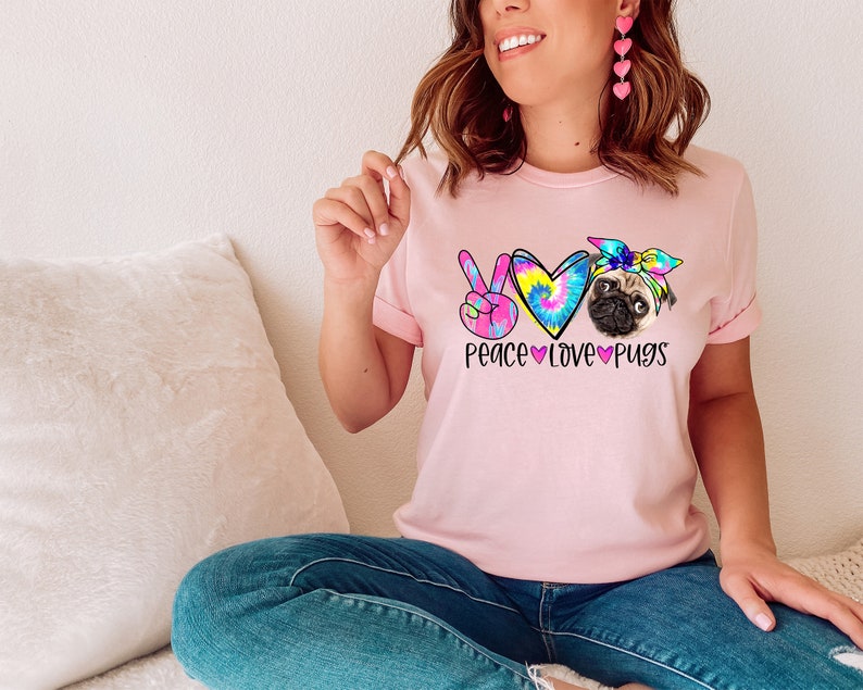 May include: A pink t-shirt with a tie-dye peace sign, heart, and pug design. The text "Peace Love Pugs" is printed below the design.