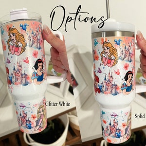 May include: Two white travel mugs with a Disney princess theme. The mug on the left is glitter white and the mug on the right is solid white. Both mugs feature a watercolor design of Cinderella, Snow White, and Belle with the Disney castle in the background.