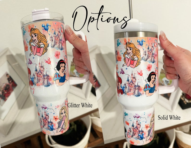 May include: Two white travel mugs with a Disney princess theme. The mug on the left is glitter white and the mug on the right is solid white. Both mugs feature a watercolor design of Cinderella, Snow White, and Belle with the Disney castle in the background.