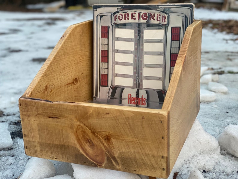 May include: A wooden record storage crate with a vintage record album inside. The album cover features a jukebox with the word "FOREIGNER" printed on it.