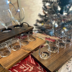 May include: A wooden serving tray with multiple glass cups and wine glasses. The tray is stained a dark brown color and has a rustic look. The glasses are arranged in rows on the tray.