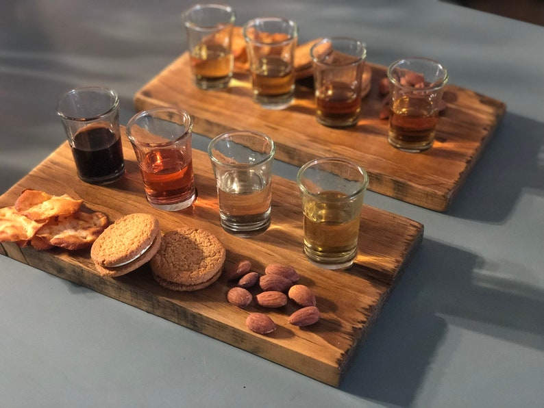 May include: A wooden serving tray with six small glasses filled with different colored liquids. The tray also has almonds, cookies, and crackers on it.