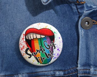 Puede incluir: Un botón redondo con una imagen de dibujos animados de labios rojos y una lengua de arcoíris. El texto "Sounds Gay I'm in!" está escrito en el botón. El botón está sobre una chaqueta vaquera azul.