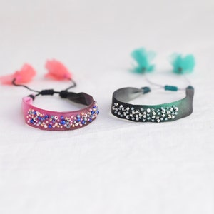 May include: Two beaded bracelets with fabric tassels. One bracelet is pink with blue and silver beads, the other is green with silver beads.
