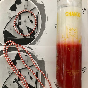 May include: Red and white beaded necklace and bracelet with a red and white candle with the word "CHANGÓ" and a butterfly design. The candle has the text "Vision Candles, Miami, FL 33147" on the bottom.