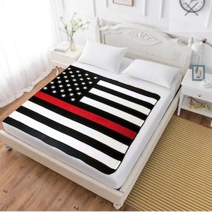 May include: A black and white American flag with a red stripe across the middle. The flag is on a white bed with white pillows.
