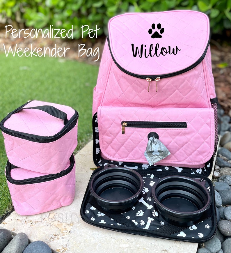 May include: Pink quilted pet carrier backpack with a paw print and the name "Willow" embroidered on the front. The backpack has two zippered compartments, a side pocket, and a black and white paw print lining. The backpack comes with two collapsible food bowls.