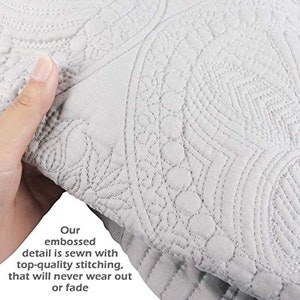 May include: Close-up of a white quilted fabric with an embossed design. The fabric has a subtle sheen and a soft texture. The text "Our embossed detail is sewn with top-quality stitching, that will never wear out or fade" is visible in the lower left corner of the image.