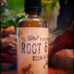 May include: A brown glass bottle with a black spray top and a label that says "ROOT & ROOM & LIFE" with a drawing of a frog and a snail. The label also has the word "PTERIDOPHYTE" on it.