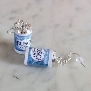 Puede incluir: Un par de pendientes de plata con un mini charm de lata de cerveza Busch Light azul y blanco en cada pendiente.