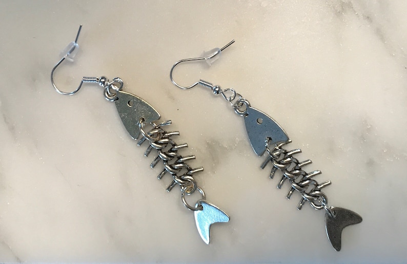 May include: A pair of silver fishbone earrings with a chain link design. The earrings are made of metal and have a hook closure.