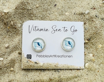 May include: A pair of earrings with a seashell design on a white card with the text "Vitamin Sea to Go" and "PebblesArtKreationen".