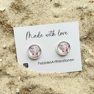 Könnte beinhalten: Ein Paar weiße Ohrstecker mit einem runden, klaren Glascabochon, der eine Aquarell-Illustration eines Elefanten zeigt. Die Karte hinter den Ohrringen lautet "Made with love" und "PebblesArtKreationen".