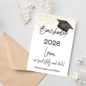Könnte beinhalten: Abschlusskarte mit schwarzem Doktorhut und goldenen Glitzerakzenten. Auf der Karte steht "Bachelor 2026 Leon, wer sind stolz auf dich! Mama, Papa und Milena" auf weißem Hintergrund, mit braunem Umschlag.