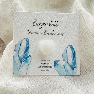 Może przedstawiać: Biały kryształ w kształcie serca na karcie z napisem "Bergkristall Talisman - Breathe easy". Karta zawiera niebieskie ilustracje kryształów i niemieckie słowa oznaczające harmonię, jasność, radość i energię.
