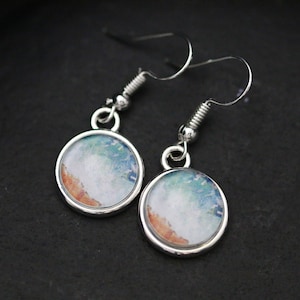 May include: A pair of silver dangle earrings with round, white, blue and orange resin cabochons. The cabochons have a watercolour-like design.