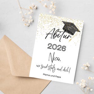 Könnte beinhalten: Eine weiße Abschlusskarte mit dem Wort "Abitur" und dem Jahr "2026" in schwarzer Schrift. Die Karte enthält auch den Namen "Nico" und eine Nachricht auf Deutsch. Oben befindet sich eine Grafik einer Abschlusskappe. Ein brauner Umschlag liegt daneben.