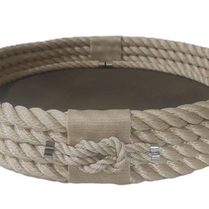 Op de afbeelding: Een ronde dienblad gemaakt van geweven beige touw met twee touwhandvatten. Het dienblad heeft een beige stoffen voering en een decoratieve knoop in het midden.